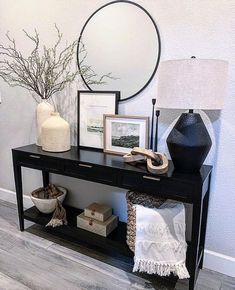 a black console table with pictures, vases and other items on it in front of a round mirror