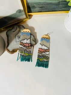 two pairs of beaded earrings sitting on top of a table next to a painting