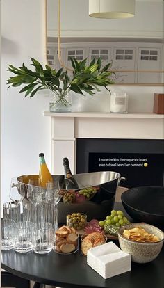 a black table topped with lots of food and wine glasses next to a fire place