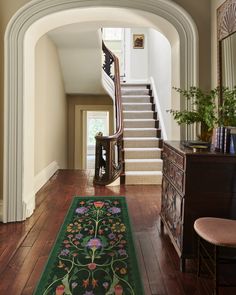 an archway leads to a foyer with a floral rug on the hardwood floor and stairs