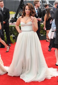 a woman in a white dress standing on a red carpet with other people around her