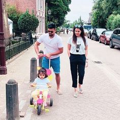 a man and woman pushing a child on a tricycle down the street with another person walking behind them