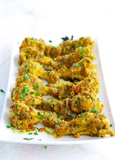 a white plate topped with chicken wings covered in sauce and green sprinkles