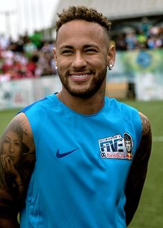 a man with tattoos on his arm standing in front of a soccer field wearing a blue shirt