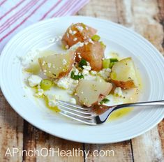 a white plate topped with potatoes and other food on top of a wooden table next to a fork