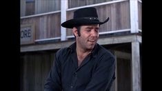 a man wearing a black cowboy hat standing in front of a building