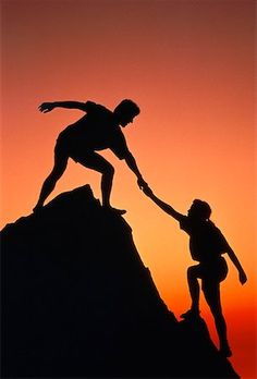 two people climbing up the side of a mountain at sunset