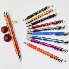 several pens and two cherries on a white surface next to each other, with one pen in the middle