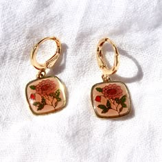 These earrings feature vintage 12mm gold plated and enamel floral charms. The 24k gold plated brass earring hoops are approx. 11mm in size. Slight color variances in the charms due to vintage nature. Charms are gold plated however some may have mild tarnishing on back due to age. Tarnish resistant hoops. Matching necklace available here. Vintage Gold Jewelry Aesthetic, Earring Hoops, Vintage Style Earrings, Vintage Nature, Jewelry Lookbook, Custom Earrings, Enamel Earrings, Delicate Earrings