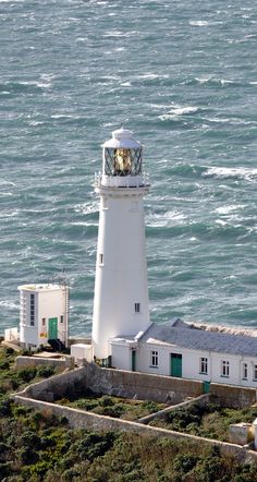 a white lighthouse sitting on top of a lush green hillside