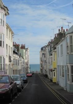 cars parked on the side of a road next to tall buildings with ocean in the background