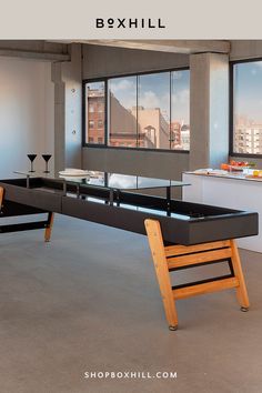 A black track dining outdoor shuffleboard table with wooden legs placed in a modern interior setting with glass windows