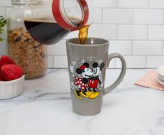 a person pours coffee into a mickey mouse mug with strawberries in the background