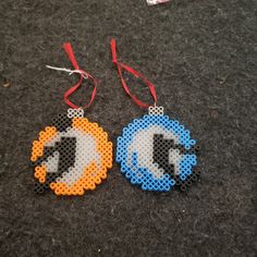 two pieces of perler bead art hanging from red string on black carpet next to each other