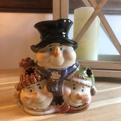 three ceramic figurines sitting on top of a wooden table next to a candle