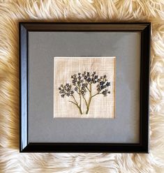 a framed art piece with some flowers in it on a furnishing area next to a wall