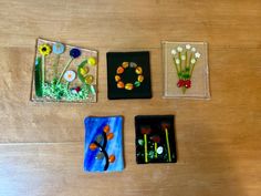 four small glass plates sitting on top of a wooden table next to flowers and beads