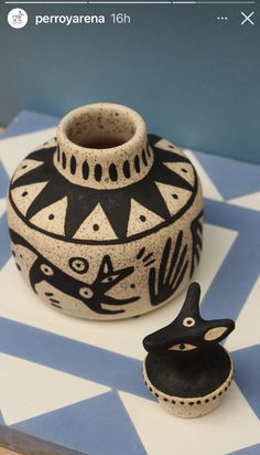 a black and white vase sitting on top of a table next to a small cup