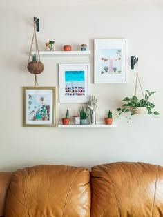 a brown leather couch sitting next to a wall with pictures and plants on top of it