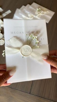 two hands holding an open white card with flowers on the front and back of it