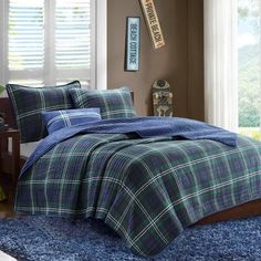 a blue and green plaid comforter set on a bed in a room with windows