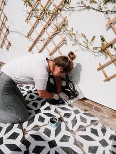 a woman kneeling down on the ground next to a white and black tiled floor with plants