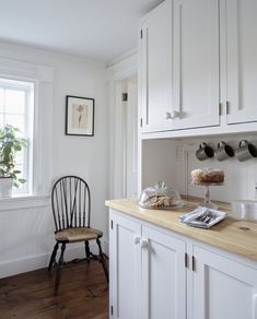 a kitchen with white cabinets and wooden counter tops, along with a black chair in front of the window