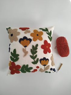 a white pillow with flowers on it next to a red ball of yarn