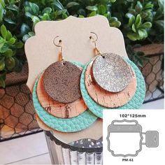 two pairs of earrings are sitting on top of each other in front of a potted plant