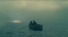 two people in a row boat on the water with fog and sun shining through the clouds