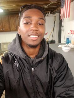 a young man in a black jacket and american flag on the back of his hat