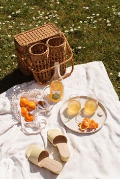 a picnic with oranges and wine on a blanket in the grass next to two wicker baskets