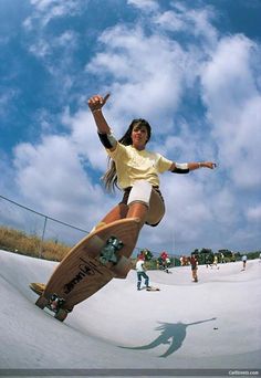 a woman riding a skateboard down the side of a snow covered slope under a blue cloudy sky