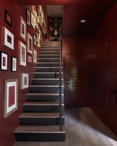 the stairs are lined with pictures and framed photographs on red walls, along with wood flooring