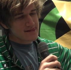 a young man holding a microphone in front of a green and black flag with the word's name on it