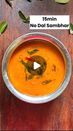 a metal bowl filled with soup on top of a wooden table next to green leaves