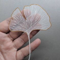 a hand holding a white string art piece in it's palm leaf like shape