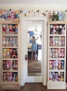 a woman standing in front of a doorway surrounded by shelves filled with dolls