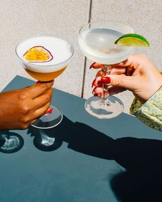 two people holding up wine glasses with drinks in them on top of a blue table