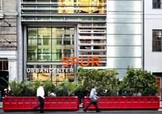 people are walking down the street in front of a large building with an orange sign