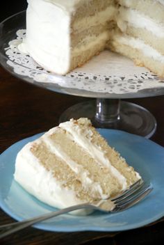 a slice of white cake on a plate with a fork next to it and the rest of the cake in the background