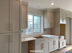 an empty kitchen with white cabinets and wood flooring in front of a large window