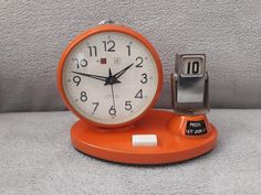 an orange alarm clock sitting on top of a table next to a silver and black phone