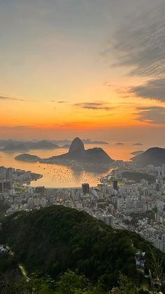 the sun is setting over a city with mountains in the foreground and water on the far side