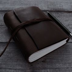 a brown leather bound book with a pen on the cover sitting on a wooden table