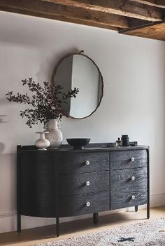 a black dresser sitting in front of a mirror on top of a wooden floor next to a white wall