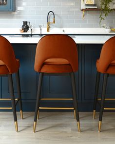 three orange chairs sitting in front of a kitchen counter