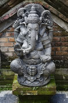 an elephant statue sitting on top of a stone block in front of a brick wall