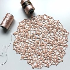 a spool of thread next to a crocheted doily