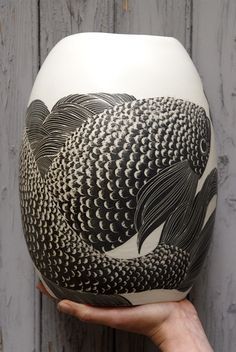 a person holding up a white vase with black fish design on the front and bottom